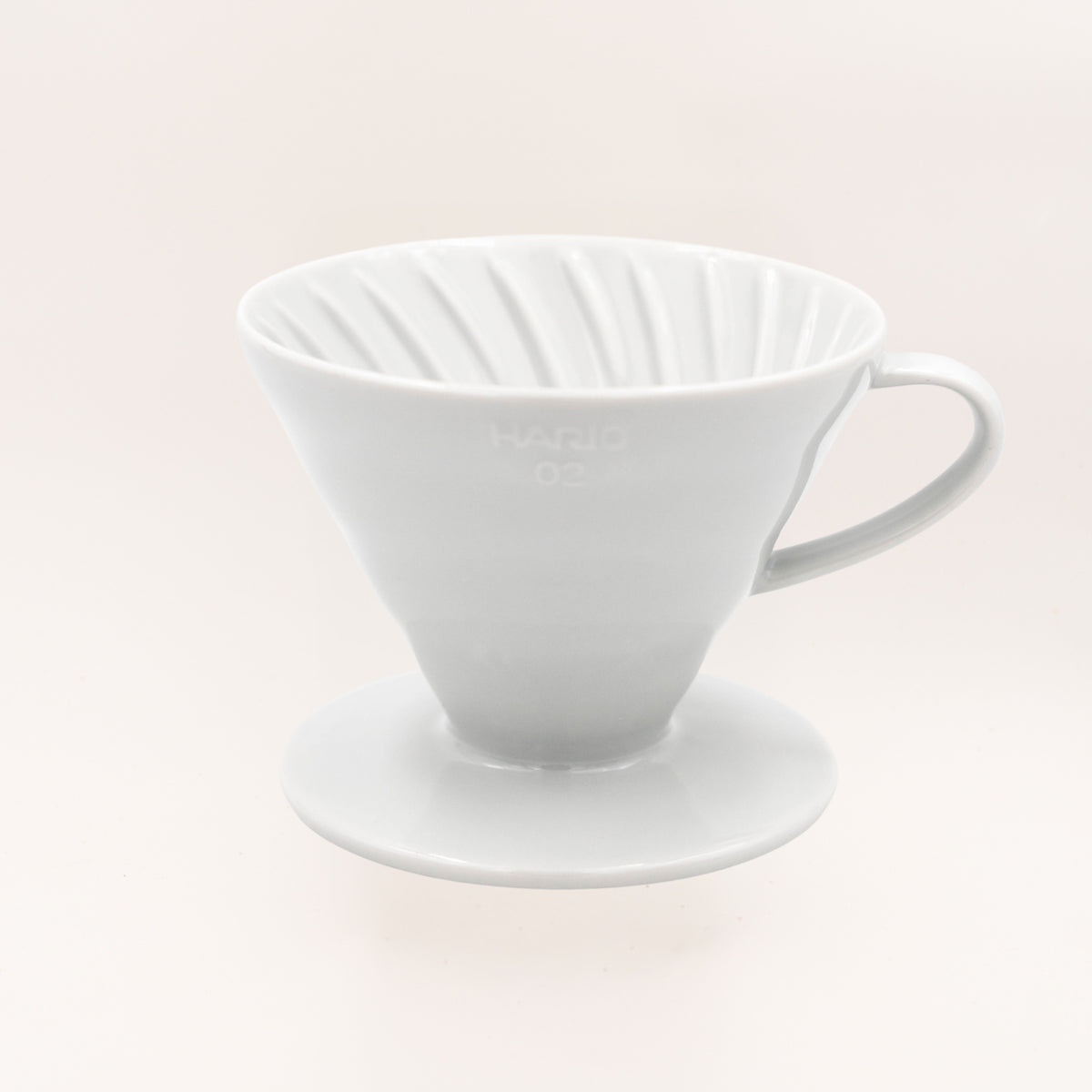A white ceramic pour-over coffee dripper with a conical shape, fluted interior, and matching saucer, shown on a clean off-white background. The brand name 'HARIO' is subtly embossed on the front.